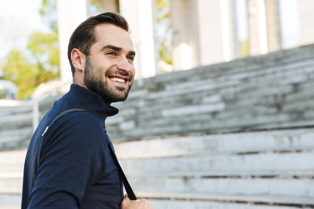 Imagen de un apuesto joven deportista fuerte feliz posando al aire libre en la ubicación del parque natural.