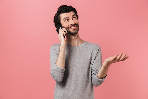 Imagen de un apuesto joven sobre pared rosa hablando por teléfono móvil.