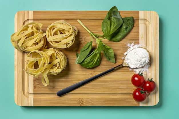 Foto imagen de arriba de los ingredientes para preparar una receta de pasta italiana y una cuchara llena de harina de trigo con un fondo completamente verde