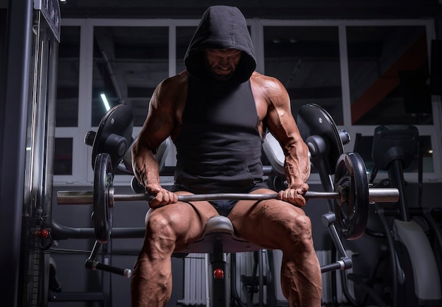 Imagen de un atleta poderoso con una sudadera con capucha sentado en un banco en un gimnasio. Concepto de fitness y culturismo. Técnica mixta