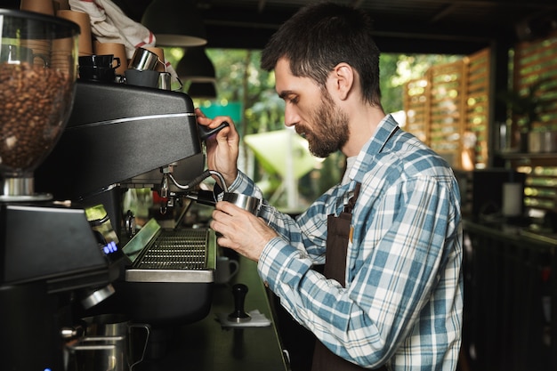 Imagen de barista profesional hombre vestido con delantal haciendo café mientras trabajaba en la cafetería o cafetería al aire libre