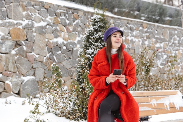 Imagen de una bella mujer joven con teléfono móvil caminando al aire libre en invierno con nieve.