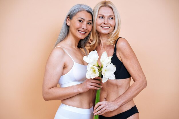 Imagen de belleza de dos mujeres con diferente edad, piel y cuerpo posando en el estudio para una sesión de fotos positiva para el cuerpo. Modelos femeninos mixtos en lencería sobre fondos de colores