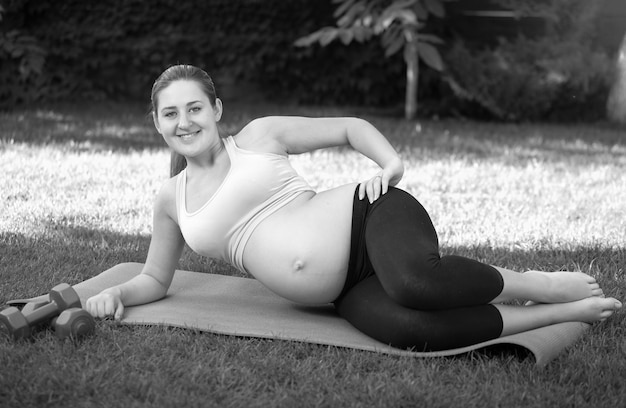 Imagen en blanco y negro de la joven futura madre que se extiende antes de yoga en el césped en el parque