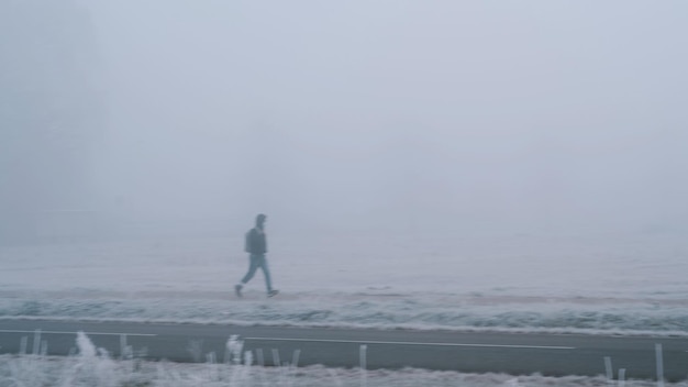 Imagen borrosa de movimiento de joven con mascarilla caminando solo en la acera en una niebla profunda