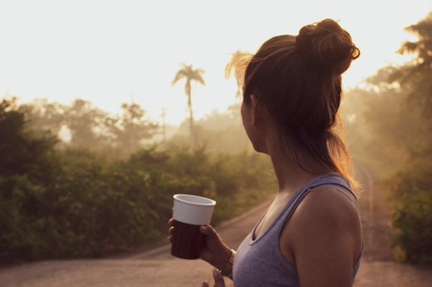 Imagen borrosa de una mujer sosteniendo una taza de café en medio de la naturaleza.