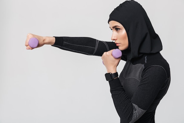 Imagen del boxeador de combate musulmán de fitness mujer joven posando aislado hacer ejercicios con pesas.