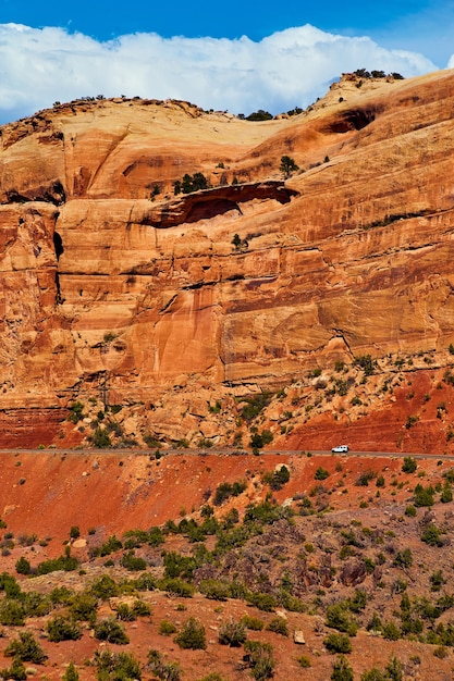 Imagen de carretera con coche cortando grandes acantilados de roca roja en el desierto