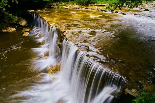 Imagen de cascadas pacíficas borde hacia arriba fluyendo hacia un río poco profundo