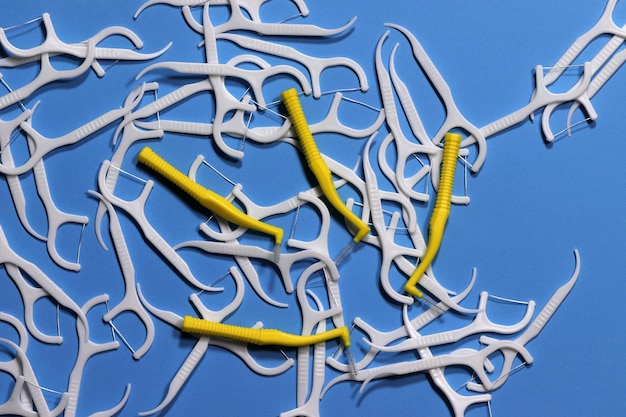 Imagen de cepillos interdentales y palillos de dientes blancos y amarillos con hilo sobre un fondo azul