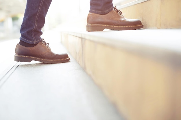 Imagen de cerca de un joven hipster con jeans azules y zapatos de cuero caminando por las escaleras de la ciudad durante el destino de viaje para crecer y aprender experiencias