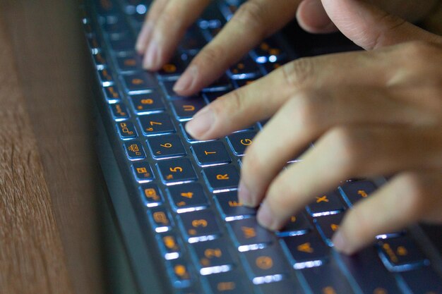 Foto imagen de cerca de las manos escribiendo en el teclado de la computadora portátil y navegando por internet en casa