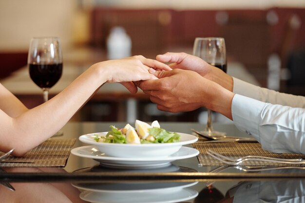 Imagen cercana de la joven pareja cogidos de la mano sobre el plato de ensalada en la mesa del restaurante