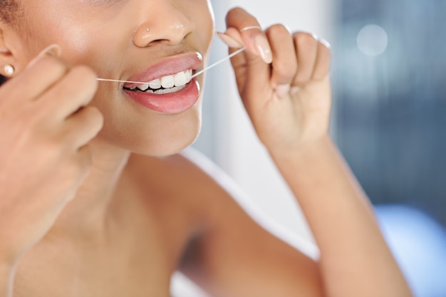Foto imagen cercana de mujer joven limpiando sus dientes blancos con hilo dental