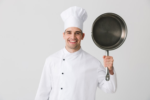 Imagen de chef emocionado joven emocional adentro aislado sobre fondo de pared blanca sosteniendo una sartén.