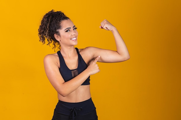 Imagen de una chica afroamericana fuerte y segura que dobla sus bíceps y lo señala.
