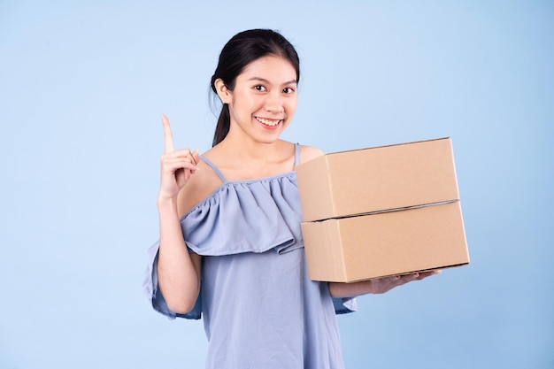 Imagen de una chica asiática sosteniendo una caja, aislado sobre fondo azul.