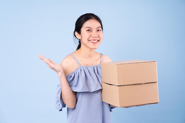 Imagen de una chica asiática sosteniendo una caja, aislado sobre fondo azul.