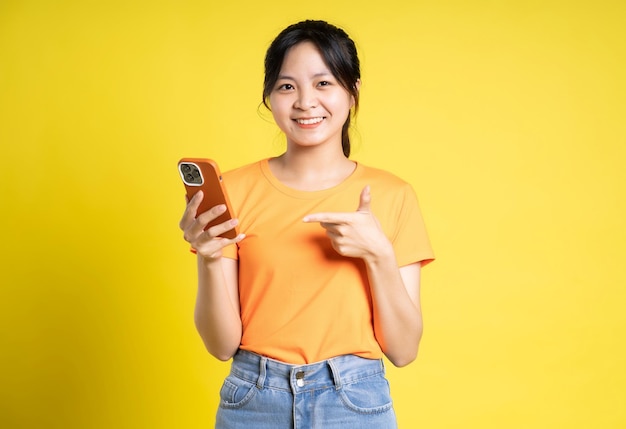 Imagen de una chica asiática usando un teléfono y aislada en un fondo amarillo