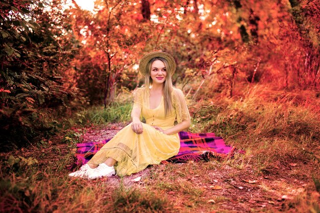 imagen de una chica con un vestido amarillo sentada en una manta en un parque de otoño