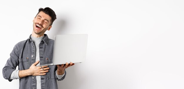 Imagen de un chico feliz riéndose de un video gracioso en una laptop tocando el vientre y sonriendo satisfecho con una buena l