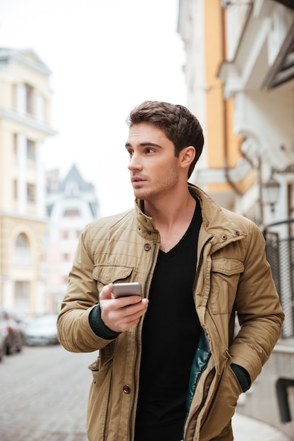 Imagen de chico guapo caminando por la calle y charlando por su teléfono al aire libre. Mira a un lado.