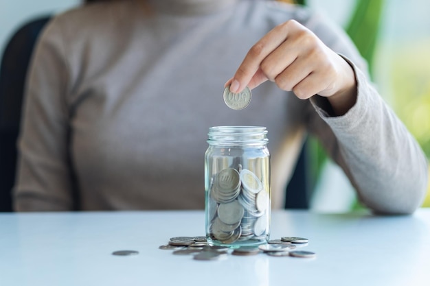 Imagen de cierre de una mano recogiendo y poniendo monedas en un frasco de vidrio para ahorrar dinero concepto