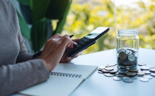 Imagen de cierre de una mujer ahorrando dinero en un frasco de vidrio calculando y tomando nota del concepto financiero