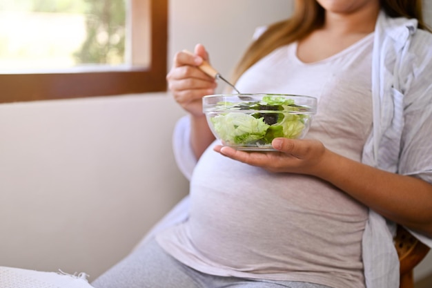 Imagen de cierre de una mujer asiática embarazada comiendo una ensalada saludable para desayunar en una mesa