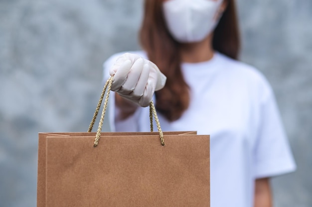 Imagen de cierre de una mujer con mascarilla protectora y guantes médicos de goma que entrega una bolsa de compras para el cliente Atención médica y concepto Covid19