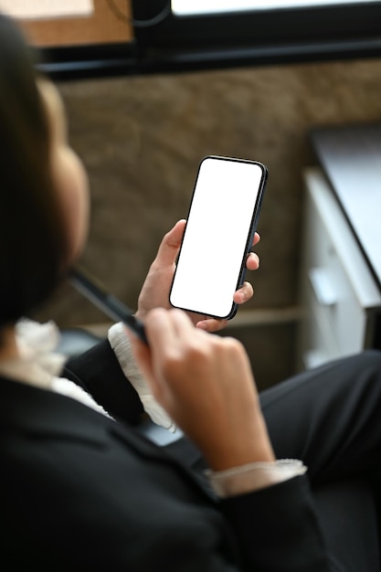 Imagen de cierre de una mujer de negocios asiática sosteniendo su teléfono inteligente mientras está sentada en su escritorio