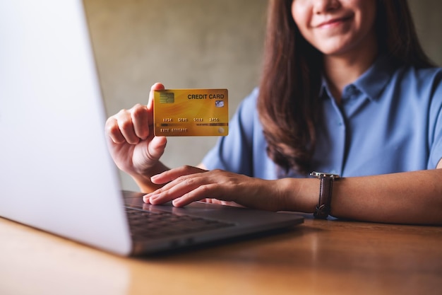 Imagen de cierre de una mujer de negocios sosteniendo y mostrando una tarjeta de crédito mientras usa una computadora portátil para el pago en línea