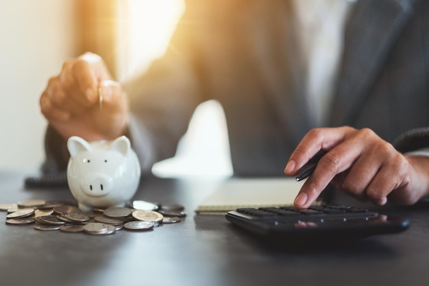 Imagen de cierre de una mujer poniendo monedas en una alcancía y calculando con calculadora para ahorrar dinero y concepto financiero