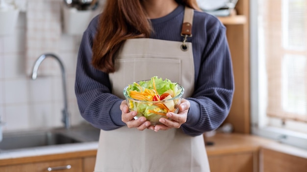 Imagen de cierre de una mujer sosteniendo y mostrando una ensalada de verduras mixtas frescas en la cocina de casa