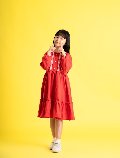 Foto imagen completa del cuerpo de una niña asiática con un vestido y posando sobre un fondo amarillo