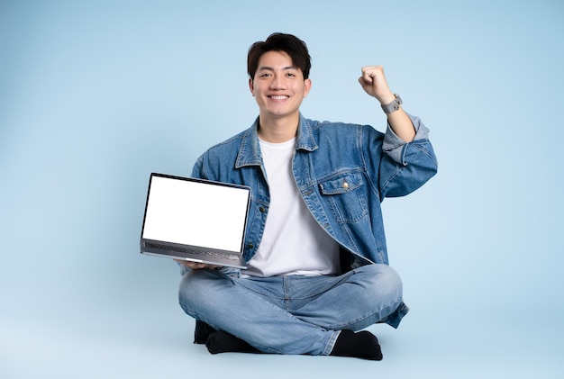 Imagen completa del cuerpo de un tipo asiático usando una computadora portátil sobre un fondo azul