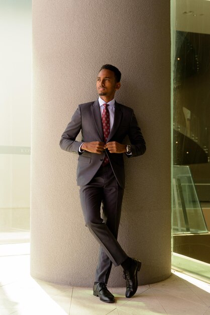 Imagen completa de un hombre de negocios africano con traje y corbata al aire libre en la ciudad mientras piensa