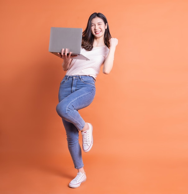 Imagen completa de una joven asiática usando una laptop con fondo naranja