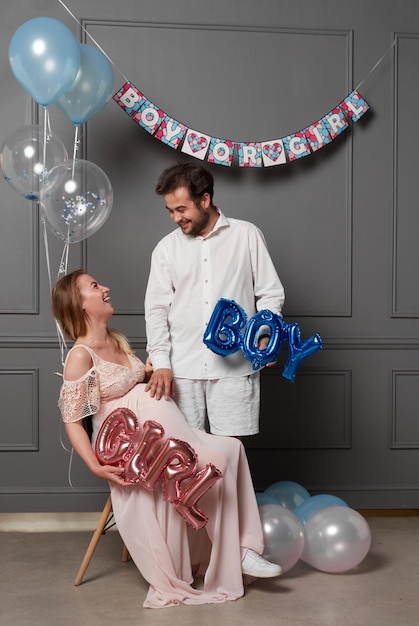 Imagen completa de una mujer y un hombre emocionados sosteniendo un globo durante una fiesta de revelación de género en el interior de una foto de estudio