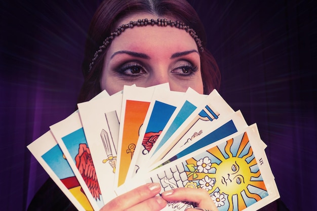 Imagen compuesta de adivino sosteniendo cartas del tarot mientras mira lejos
