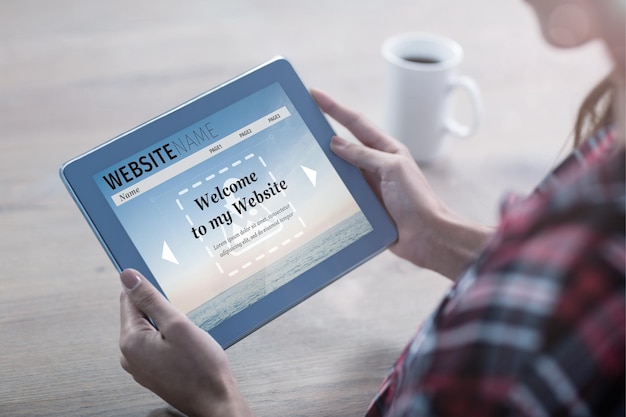Imagen compuesta de construir la interfaz del sitio web contra la mujer que usa la tableta en una mesa