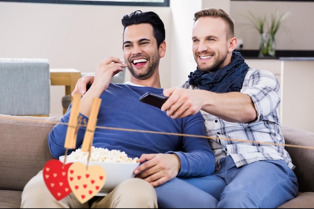 Imagen compuesta de corazones colgantes rojos y amigos viendo la televisión en el salón