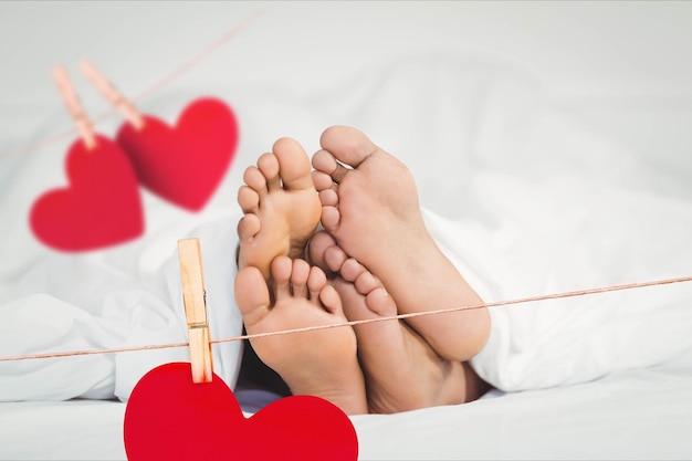 Imagen compuesta de corazones colgantes rojos y pareja acostada en la cama