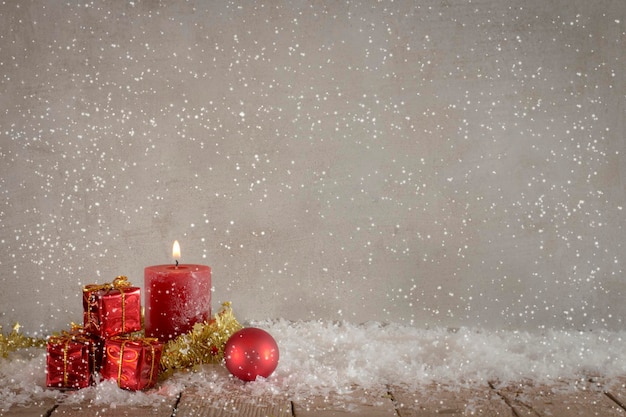 Imagen compuesta digital de regalos de Navidad y vela con nieve falsa contra la pared en la mesa