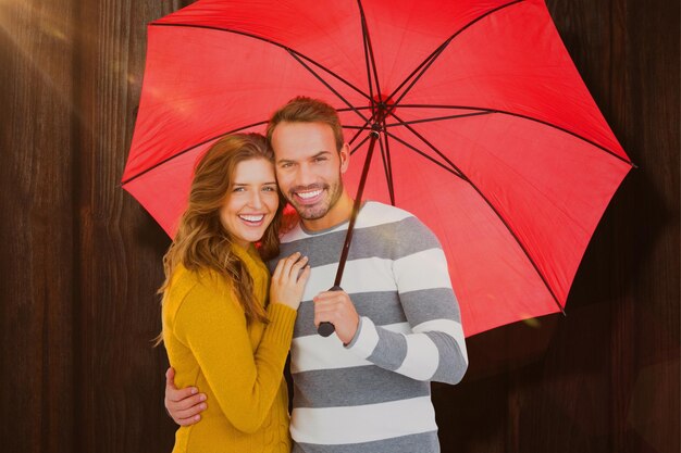 Imagen compuesta de feliz pareja joven sosteniendo paraguas rojo