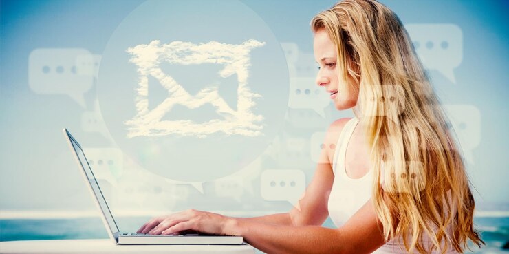 Foto imagen compuesta de una guapa rubia usando su laptop en la playa con la mano presentando un correo electrónico en la nube
