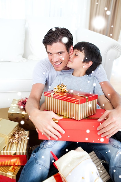 Imagen compuesta de hijo besando a su padre después de recibir un regalo de Navidad con nieve cayendo