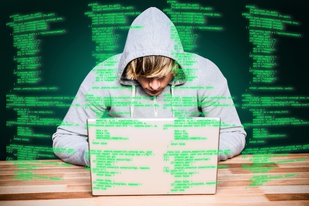 Imagen compuesta de hombre con capucha hackeando una laptop