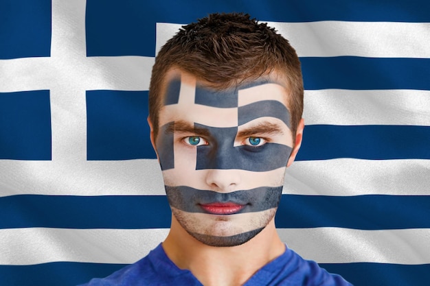 Imagen compuesta de un joven fan serio de Grecia con pintura facial contra la bandera nacional griega generada digitalmente