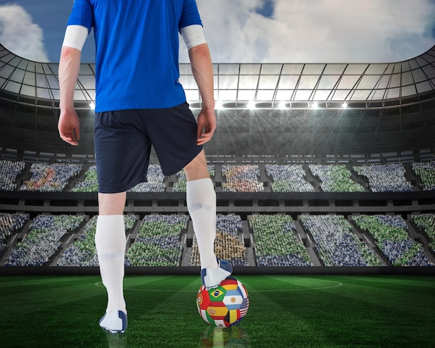 Imagen compuesta de un jugador de fútbol de pie con un balón de bandera contra un gran estadio de fútbol bajo focos